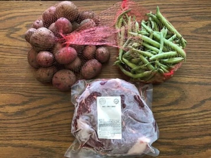 Holly+Koeppe+-+IMG_3650 Fresh produce and meat arrangement featuring a bag of beef, a bundle of green beans, and a pile of red potatoes on a wooden surface.